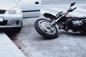 Motorcycle lying on the road after accident beside a car with an open door