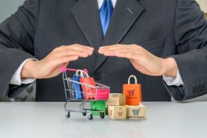 A man in a suit using his hands to cover a mini shopping cart representing the concept of Product Liability