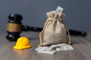 A bag of money, a gavel and a construction helmet illustrating the concept of Workers' Compensation